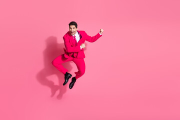 Energetic young man in a pink suit jumping joyfully on a solid pink background, inspiring fun and confidence