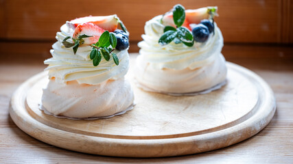 Homemade meringue desserts topped with fresh strawberries and blueberries, elegantly presented on a wooden board, showcasing delightful bakery craftsmanship and vibrant colors