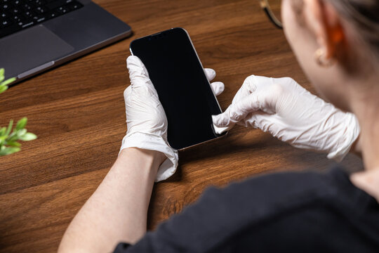 Person in white protective gloves thoroughly cleaning a smartphone screen, promoting essential hygiene and virus protection in a modern digital world