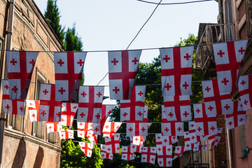 View of Georgian flags strung across a narrow street, creating a vibrant display of red and white against the backdrop of old buildings, Tatev, Syunik Province, Armenia.