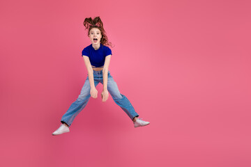 Cheerful young woman in stylish casual outfit jumping against a vibrant pink backdrop, expressing energy and excitement