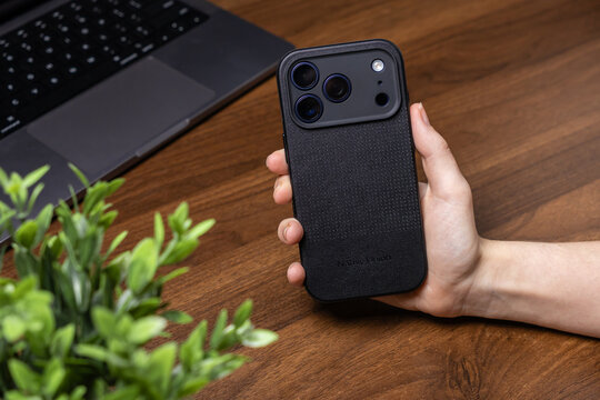 Poznan, Poland - October 16, 2025: iPhone 17 Pro, Native Union black textured protective case, held by hand on a wooden desk, symbolizing modern mobile tech