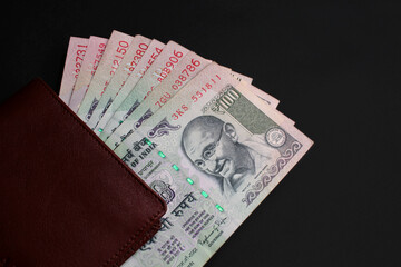 Closeup image of old Indian 100 rupee notes (INR) in brown leather wallet on black surface, top view. Concept of cash savings, financial profit and security, Indian economy.