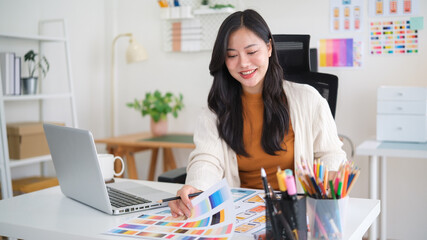 Smiling UX UI designer working on color palettes and mobile app interface mockups at modern office desk.