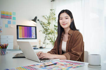Young creative professional smiling while working on laptop in modern design studio.