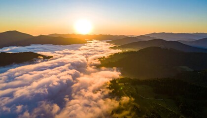Sunrise over mountainous landscape with valley filled with low-lying clouds & green slopes