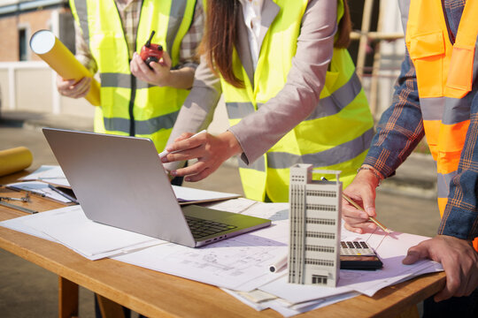 Architectural team analyzing structure plans and digital drawings on site. Concept of teamwork and construction development. - Powered by Adobe