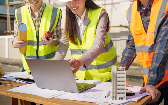Architectural team analyzing structure model and project drawings at construction area.