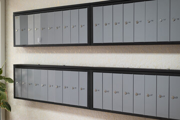 Gray metal wall-mounted mailboxes with individual locks and numbers in an apartment or office building lobby.