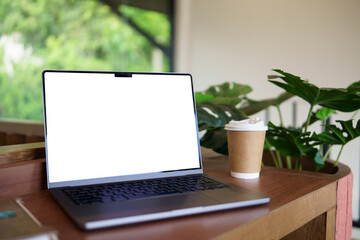 Fototapeta premium Laptop with blank white screen on wooden table beside takeaway coffee cup. Concept of remote work, and mockup design.