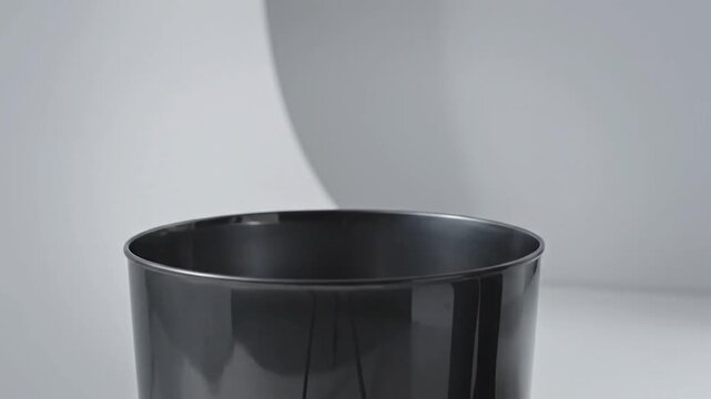 A hand prepares to toss a crumpled paper ball into a dark, metallic trash can