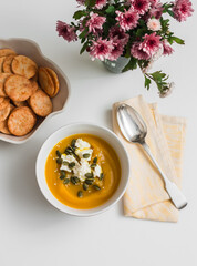 Delicious autumn lunch - pumpkin soup with cottage cheese, pumpkin seeds, cheese cracker, bouquet of chrysanthemums on a light background, top view