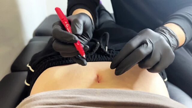 Сlose-up video of piercer in black gloves marking the exact point for a belly button piercing with red sterile marker. Focus on preparation, accuracy,hygiene, and professional technique in clean salon