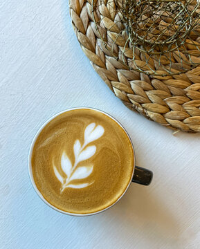 Flat lay overhead view of cup of cappuccino coffee with leaves design next to a textured table decoration during Fall time suitable for background with copy space. 