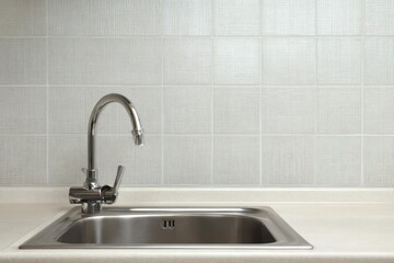 Stainless steel sink and faucet against a tiled wall.