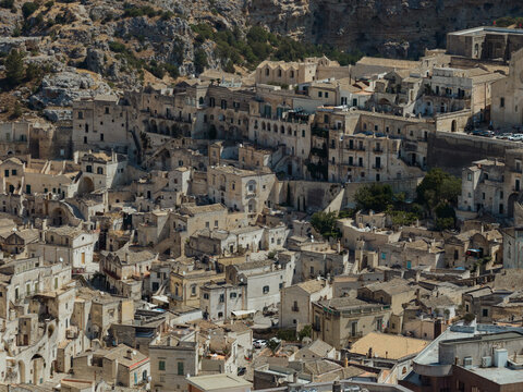 Aerial view of ancient dwellings cascade down the rocky slopes, a symphony of beige and umber hues under the bright Italian sun, Matera, Basilicata, Italy.