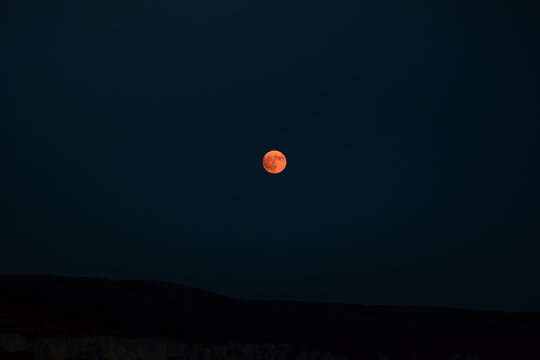 Aerial view of a lone, fiery moon glows against the inky sky, its orange hue contrasting with the darkness, Matera, Basilicata, Italy.