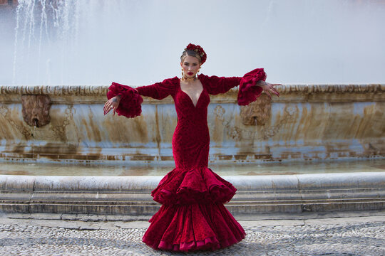 A beautiful woman dancing flamenco in a square in Seville, Spain. She is wearing a red dress with ruffles and dancing flamenco with great artistry. Flamenco, cultural heritage of humanity.