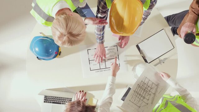 Top view of diverse construction team analyzing structural drawings on table. Concept of collaboration, leadership, accuracy in engineering and architectural teamwork.