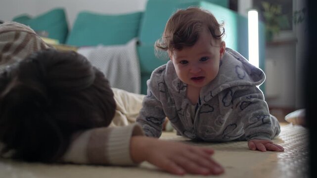 Baby on floor beside older brother, looking concerned and uncertain, showing mild discomfort and emotional sensitivity in warm family home environment