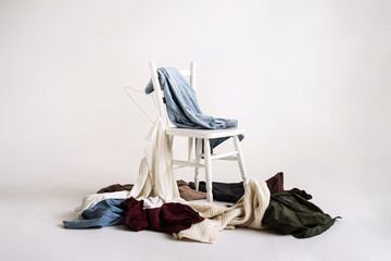 Wrinkled women's clothes scattered on the floor and a chair. Clothing sorting and storage. Minimalistic mockup on a white background.