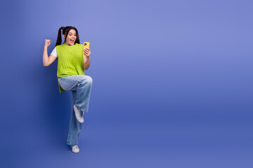 Young woman in bright green sweater taking a selfie with smartphone against blue background smiling...