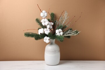 Beautiful composition with fir tree branches in vase on white marble table near light brown wall indoors. Winter decor