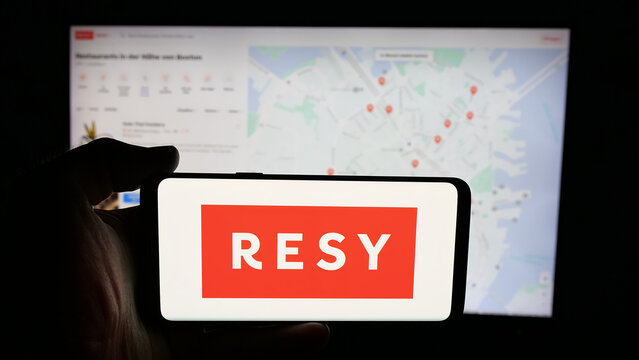 Stuttgart, Germany - 10-18-2025: Person holding cellphone with logo of US restaurant reservation company Resy on screen in front of webpage. Focus on phone display.