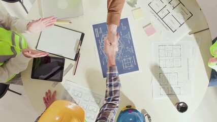 Close overhead of handshakes between engineers over building blueprints on table. Concept of partnership, success, professional agreement in architecture and construction teamwork.
