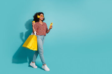 Young woman with yellow accessories shopping bag headphones and phone posing against bright blue background for fashion lifestyle promotional image