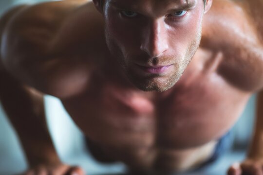 Muscular man performing push ups with intense concentration, focusing on fitness and body strength in a gym workout