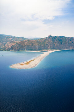 Aerial view of the sandy spit stretching into the deep blue sea, contrasting with the rugged, arid mountains in the background, Marinello, Citt&agrave; metropolitana di Messina, Italy.