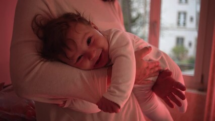 Baby resting in mother’s arms, looking relaxed and secure in warm natural light near kitchen window