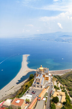 Aerial view of the golden-domed Basilica Santuario Maria del Tindari perched atop a cliff, where the sandy beach curves into the azure sea, Marinello, Citt&agrave; metropolitana di Messina, Italy.