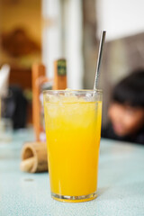 A glass of fresh orange juice with ice cubes and a stainless steel straw on a table, refreshing tropical drink perfect for summer.