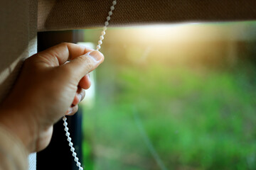 Hand pulls the rope to open the curtains to let in the morning sunlight.
