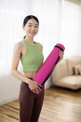 Smiling Asian Middle-Aged Woman in Activewear Holding Yoga Mat Indoors