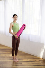 Smiling Asian Middle-Aged Woman in Activewear Holding Yoga Mat Indoors