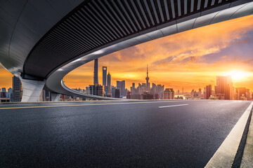 Empty asphalt road under a modern overpass with the city skyline at sunrise in Shanghai.