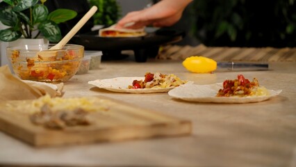 A young woman is preparing a tasty quesadilla with ingredients like cheese and peppers in a modern kitchen setting.