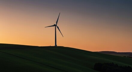 Wind turbine silhouetted atop a grassy hill against a warm sunset sky