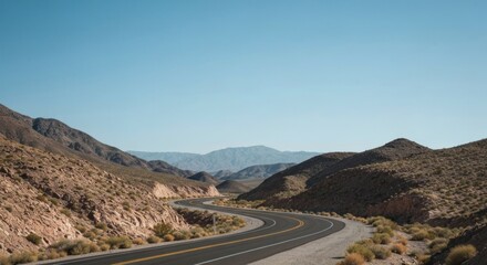 Winding road cuts through arid, rocky hills beneath a clear blue sky