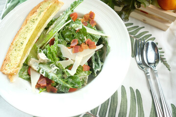 Delicious Caesar salad in a white bowl with bread and cutlery. This culinary creation features fresh ingredients, beautifully presented for a satisfying meal