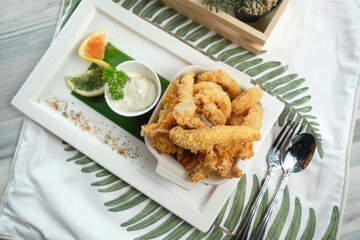 Golden fried calamari and dipping sauce on a rectangular white plate and table setting. This food photography showcases the appetizing and delicious seafood dish