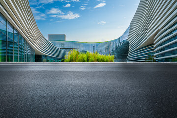 Empty asphalt road in front of a modern futuristic office building with a curved glass facade.