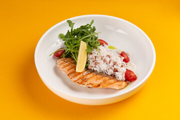 Salmon steak and rice in a plate on a yellow background.