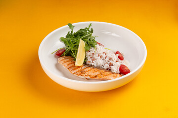 Salmon steak and rice in a plate on a yellow background.