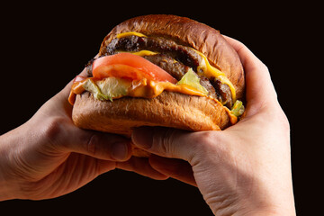 A delicious cheeseburger in hands against a dark background.