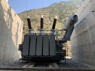 Large, outdoor three-phase power transformer with high-voltage bushings, set against a steep,...