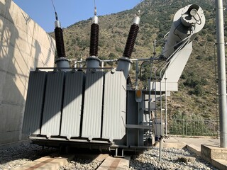 Large, outdoor three-phase power transformer with high-voltage bushings, set against a steep,...